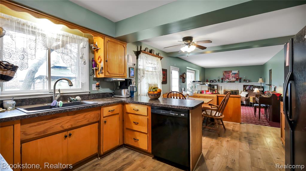 Kitchen with dark countertops, a peninsula, black appliances, dark wood-style floors, and beam ceiling
