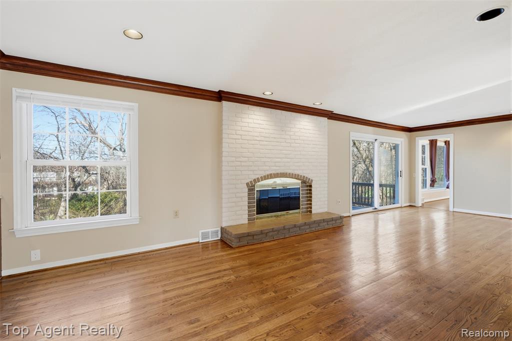 Unfurnished living room with a brick fireplace, ornamental molding, light wood-style flooring, and recessed lighting