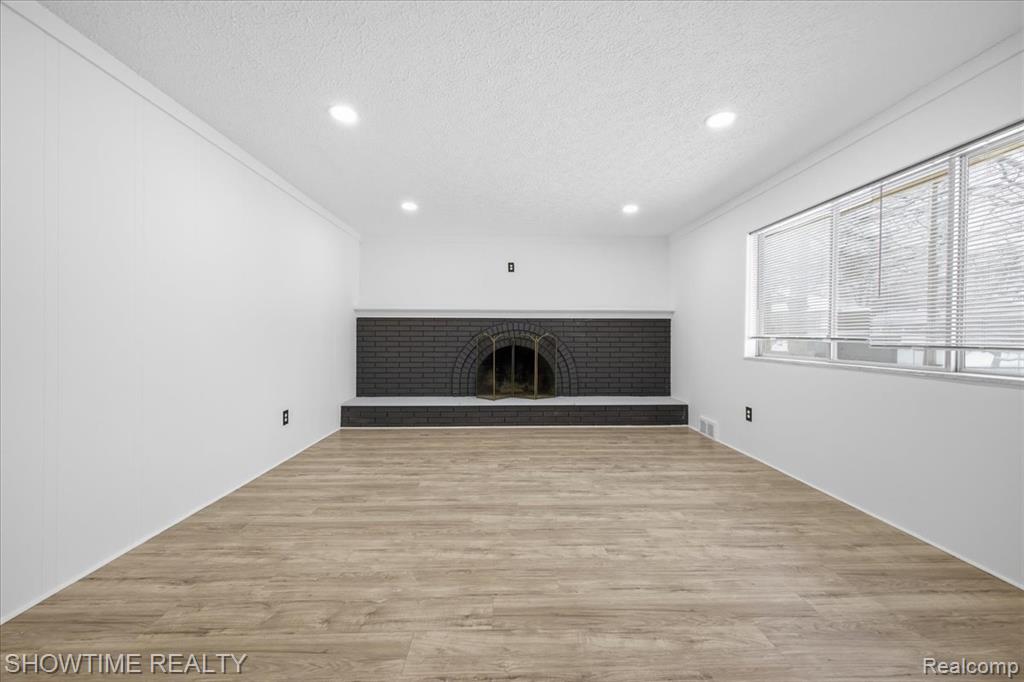 Unfurnished living room with a brick fireplace, light wood-type flooring, recessed lighting, a textured ceiling, and ornamental molding