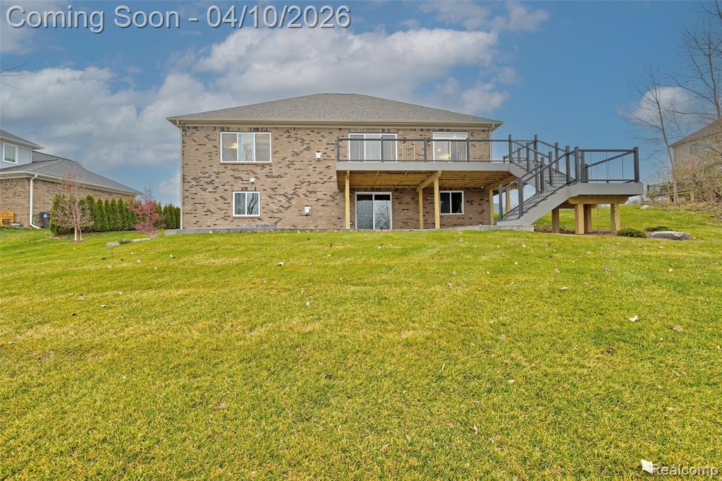 Rear view of property featuring brick siding, a wooden deck, a patio area, and a yard