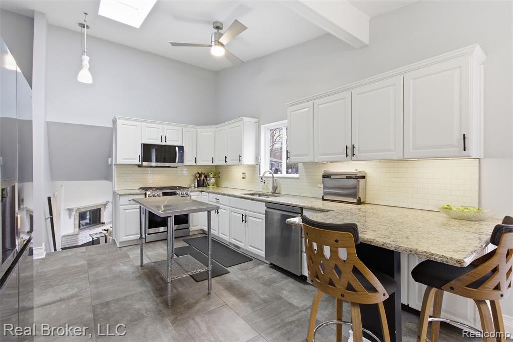 Kitchen with a breakfast bar area, white cabinetry, stainless steel appliances, a skylight, and a peninsula