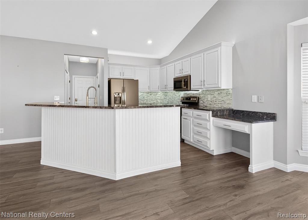 Kitchen featuring white cabinetry, a center island with sink, tasteful backsplash, vaulted ceiling, and stainless steel appliances