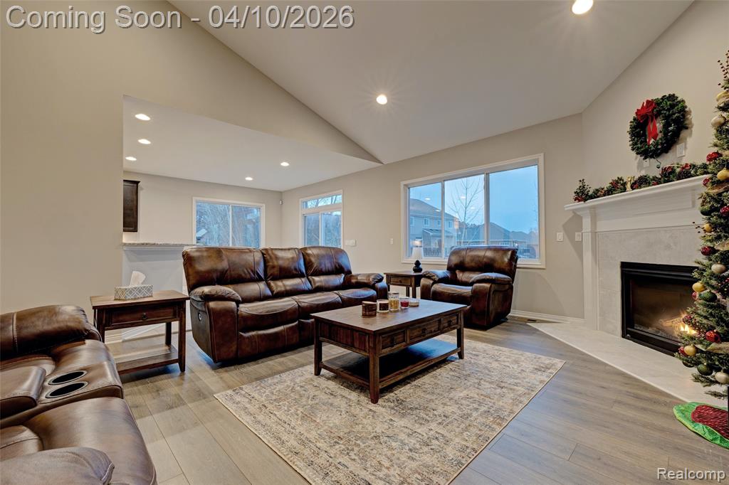Living area with lofted ceiling, light wood-type flooring, a high end fireplace, and recessed lighting