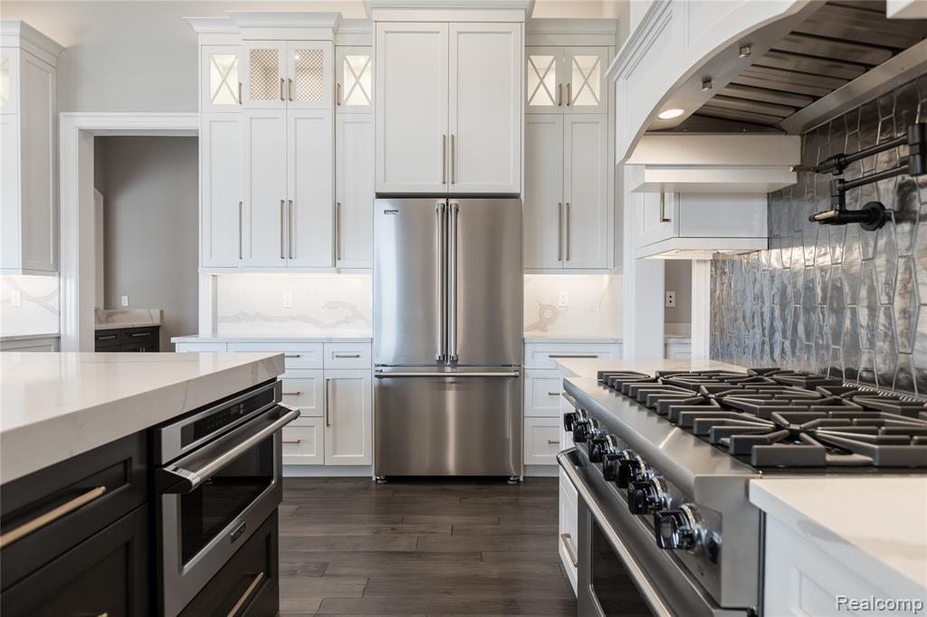 Dual tone kitchen with premium appliances, decorative backsplash, light stone counters, dark wood-style floors, and two tone cabinets