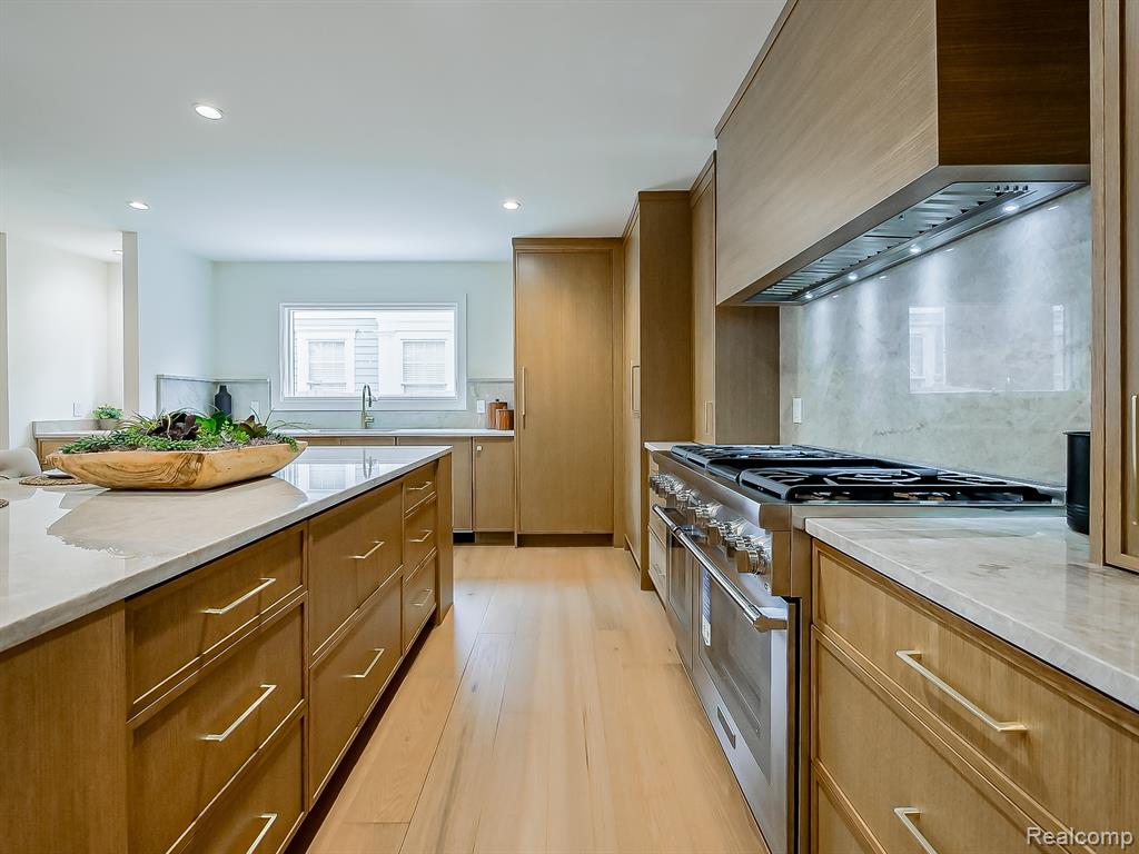 Kitchen featuring range with two ovens, custom exhaust hood, light stone countertops, light wood-style flooring, and recessed lighting