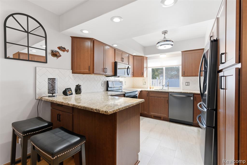 Kitchen with a peninsula, a breakfast bar area, light stone countertops, recessed lighting, and stainless steel appliances