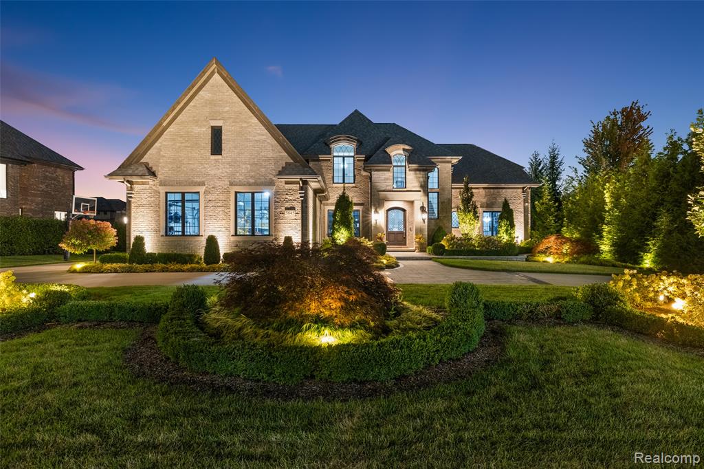 Brick exterior with arched entry, gabled roofline, multiple windows, circular driveway, and extensive landscaping
