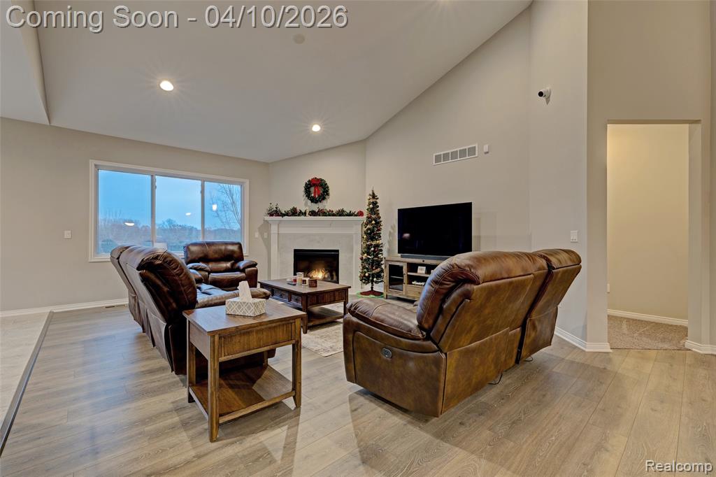 Living room with light wood finished floors, a warm lit fireplace, lofted ceiling, and recessed lighting