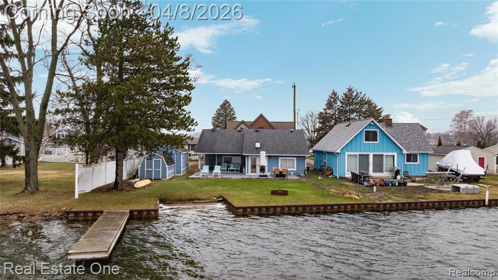 Back of property featuring a patio, a water view, a shed, roof with shingles, and an outdoor fire pit