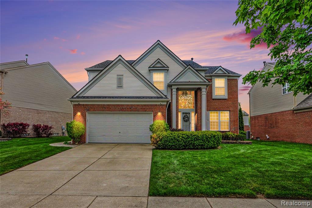 View of front of home with a yard, driveway, and brick siding