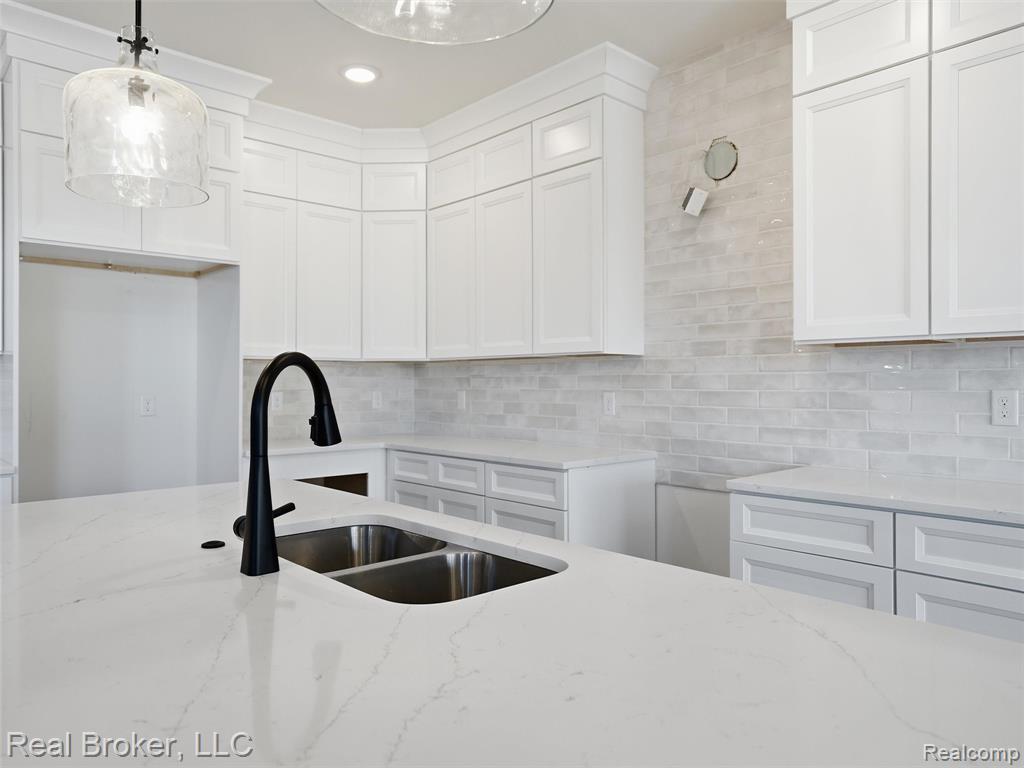 Kitchen featuring light stone counters, pendant lighting, and white cabinetry