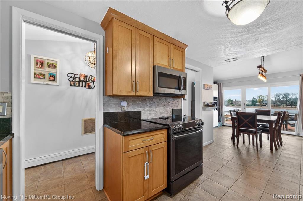 Kitchen featuring black electric range oven, stainless steel microwave, tasteful backsplash, light tile patterned floors, and dark stone countertops