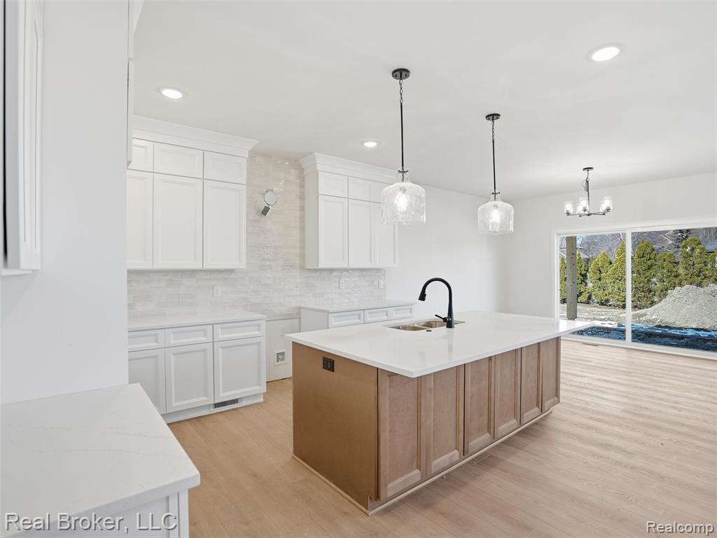 Dual tone kitchen featuring dual tone cabinets, light stone counters, an island with sink, light wood-style flooring, and backsplash