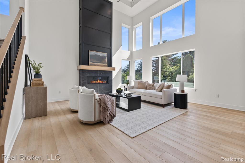 Living area featuring a tile fireplace, light wood-style flooring, a towering ceiling, and stairs