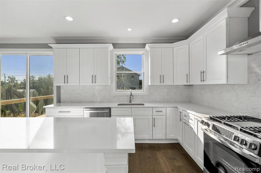 Kitchen featuring appliances with stainless steel finishes, wall chimney range hood, white cabinetry, tasteful backsplash, and ornamental molding