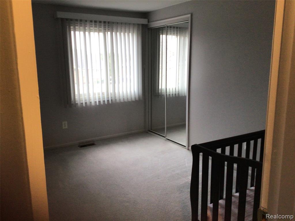 Unfurnished bedroom featuring light carpet, multiple windows, a closet, and a crib