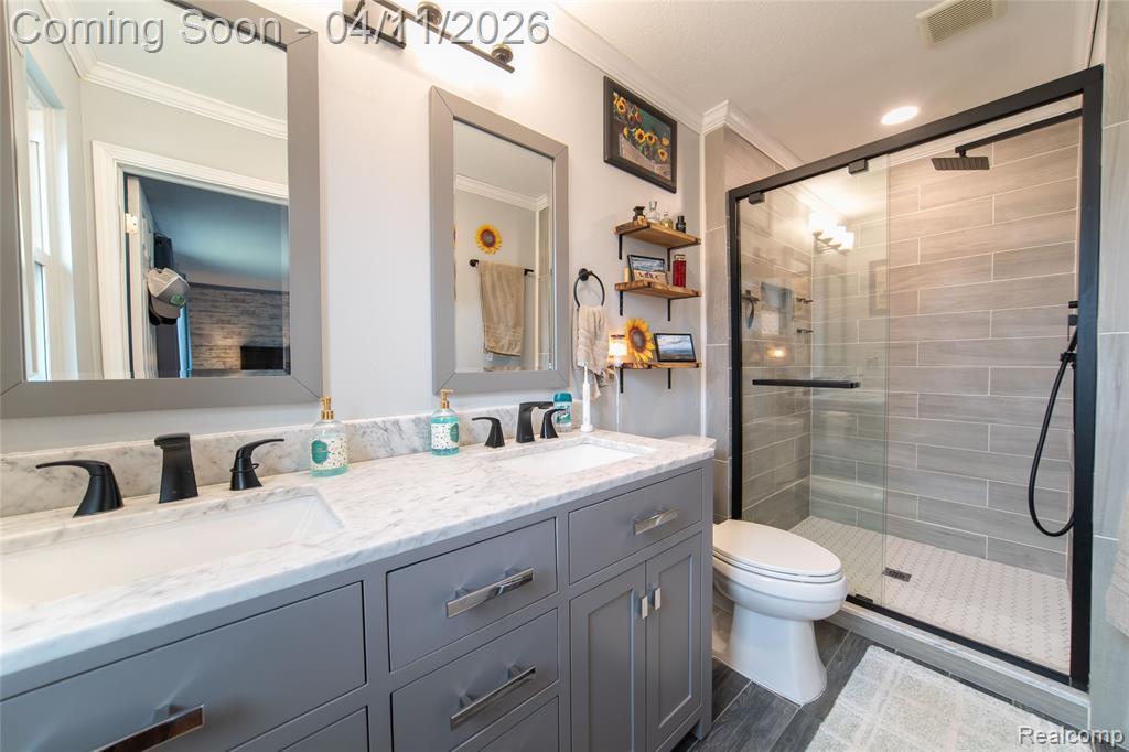 Full bathroom featuring double vanity, a stall shower, ornamental molding, and dark wood-style floors