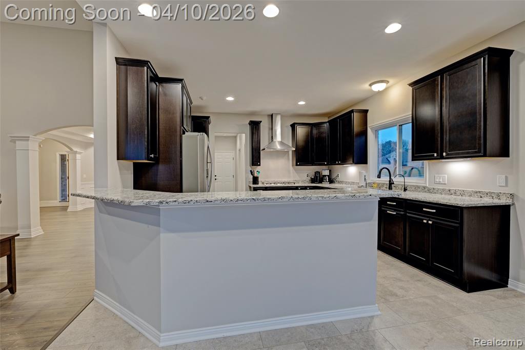Kitchen featuring arched walkways, light stone countertops, freestanding refrigerator, a peninsula, and dark wood finish cabinets