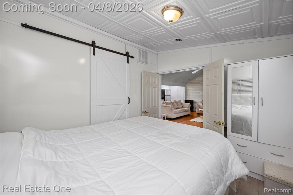 Bedroom with a barn door, an ornate ceiling, freestanding refrigerator, and wood finished floors