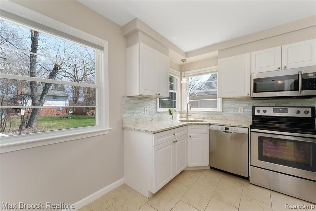 Kitchen with stainless steel appliances, light stone countertops, white cabinetry, light marble finish floors, and backsplash