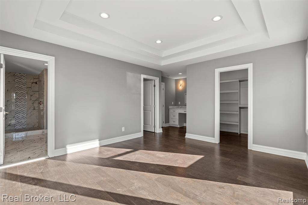 Unfurnished bedroom with connected bathroom, a walk in closet, recessed lighting, dark wood-type flooring, and a raised ceiling