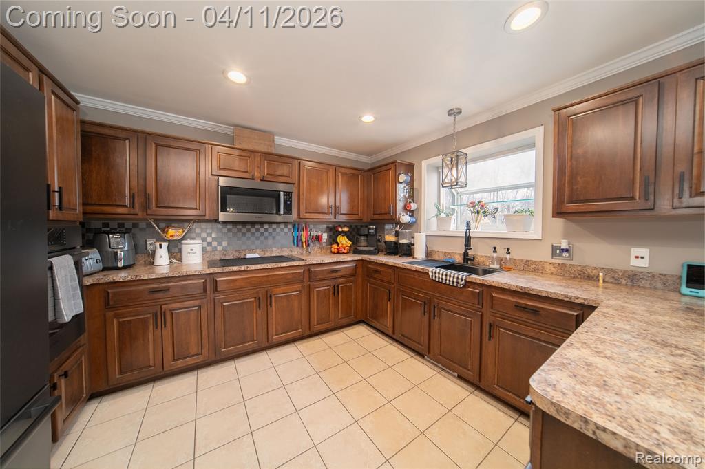 Kitchen with decorative light fixtures, light countertops, black appliances, ornamental molding, and tasteful backsplash