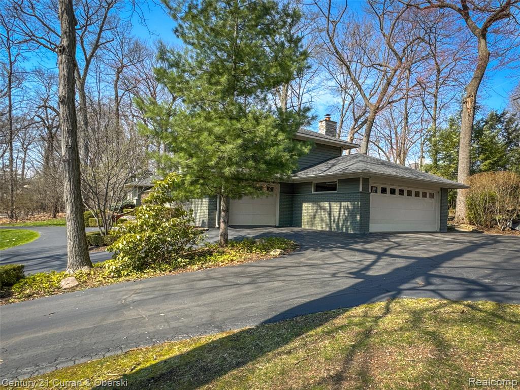 View of front facade featuring a garage, brick siding, a chimney, and driveway