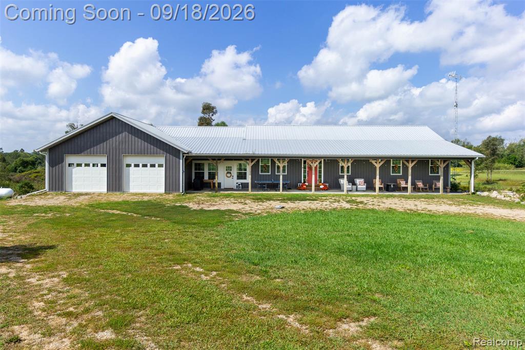 Barn-style structure with a metal roof, two white garage doors, a covered front porch, and exposed wood porch columns