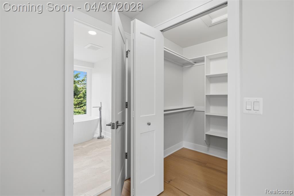 Walk in second primary bedroom closet with light wood flooring
