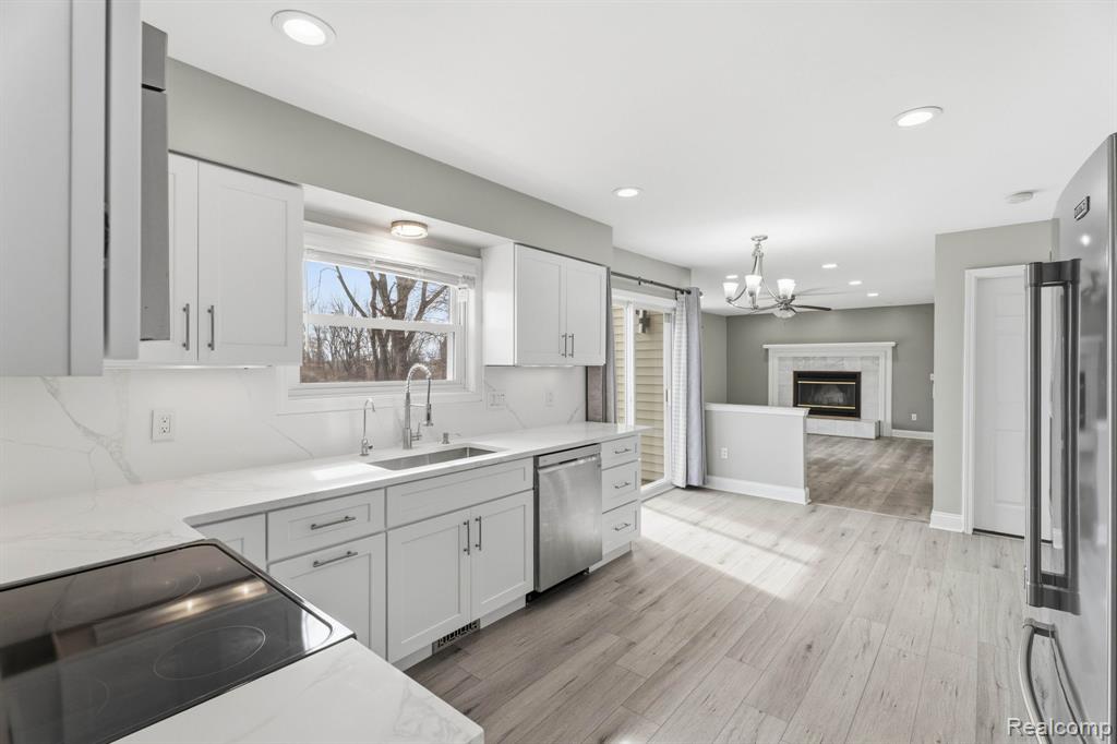 Kitchen with light wood finished floors, white cabinetry, stainless steel appliances, and light stone countertops