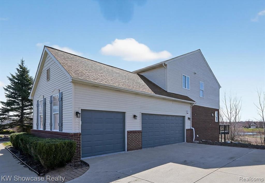 View of side of property with brick siding, an attached garage, concrete driveway, and a shingled roof