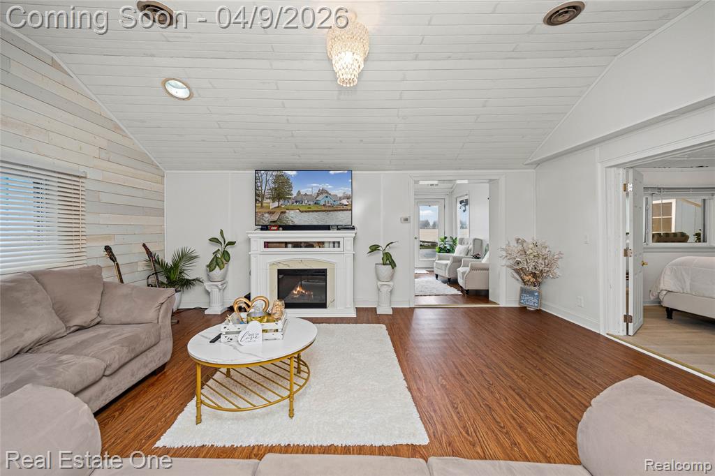 Living room featuring wood finished floors, a glass covered fireplace, and a vaulted wood ceiling