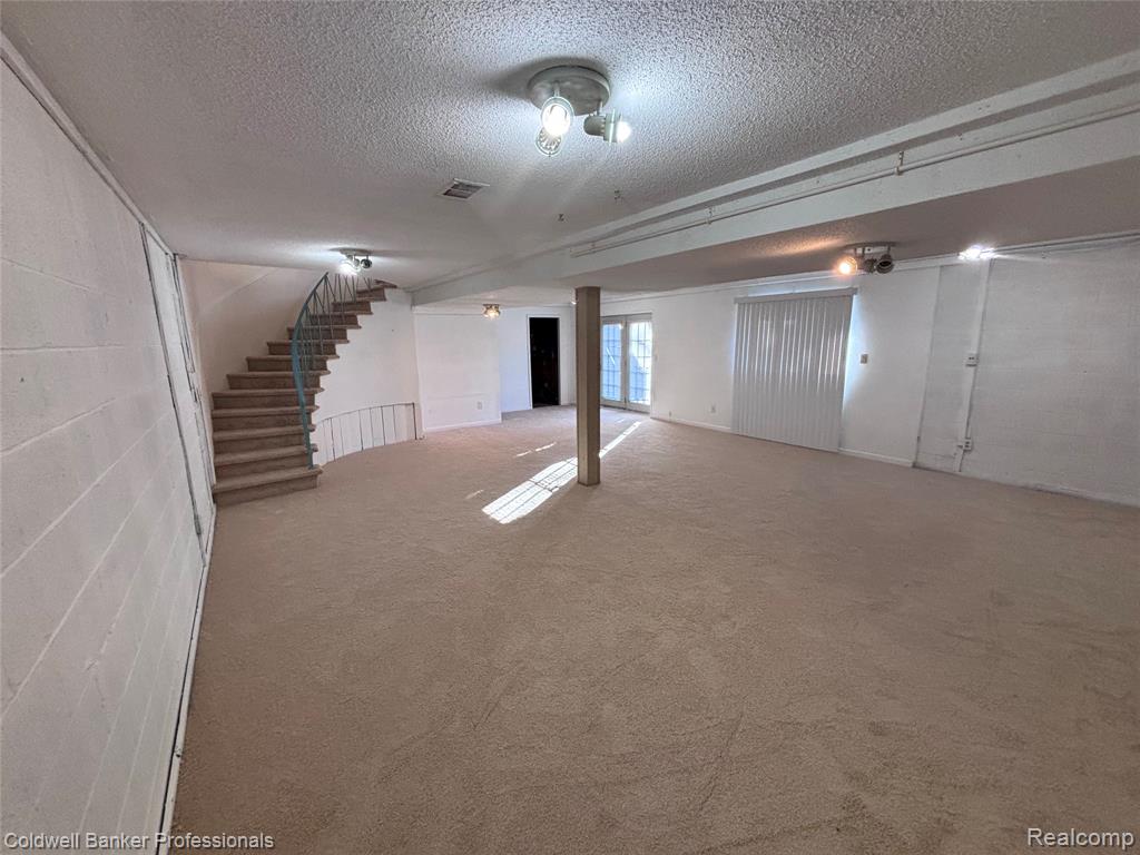 Basement featuring concrete block wall, a textured ceiling, carpet flooring, and stairs