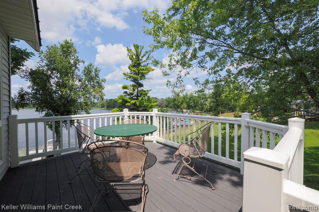 Expansive outdoor deck with sturdy white railings and dark-toned decking, overlooking a serene body of water with lush greenery along the banks