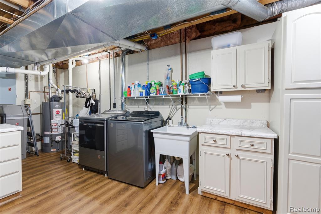 Laundry area with cabinet space, light wood-type flooring, gas water heater, and washing machine and clothes dryer