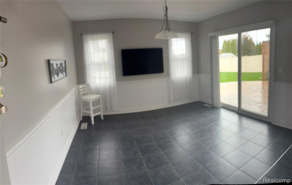 Unfurnished dining area with a wainscoted wall and dark tile patterned floors
