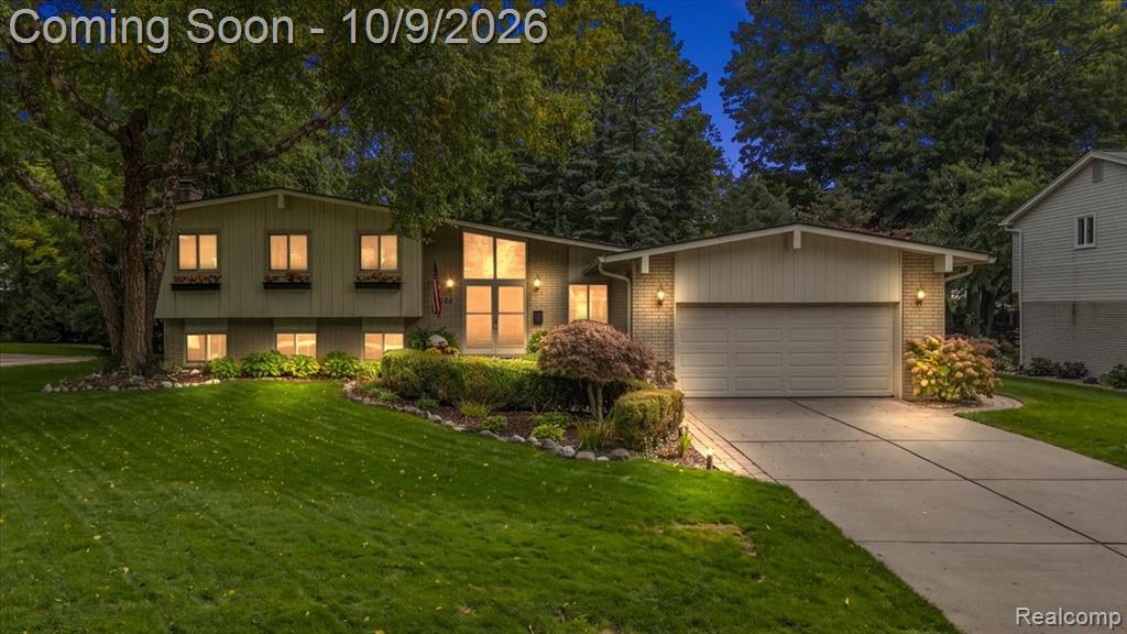 Split-level residence featuring a two-car garage, mature landscaping, and an expansive front lawn