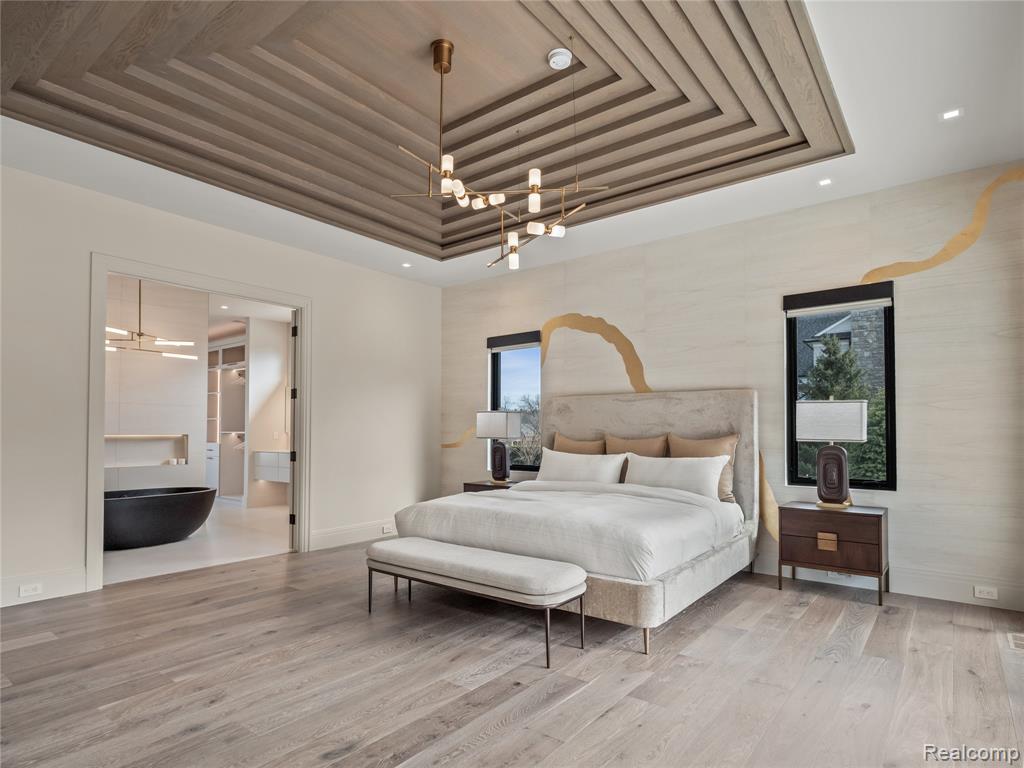Bedroom with a tray ceiling, light wood-style flooring, recessed lighting, a chandelier, and ensuite bath