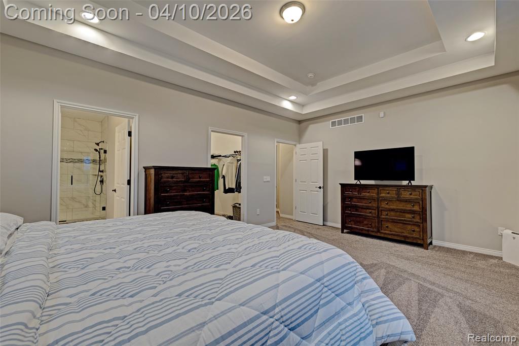 Carpeted bedroom featuring a spacious closet, recessed lighting, ensuite bath, and a raised ceiling