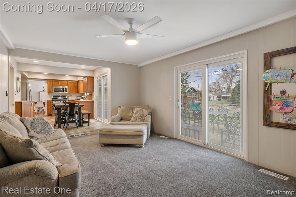 Living room featuring a ceiling fan, light carpet, and ornamental molding