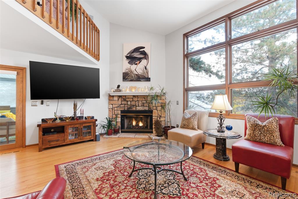 Living area with wood finished floors, healthy amount of natural light, a fireplace, and vaulted ceiling