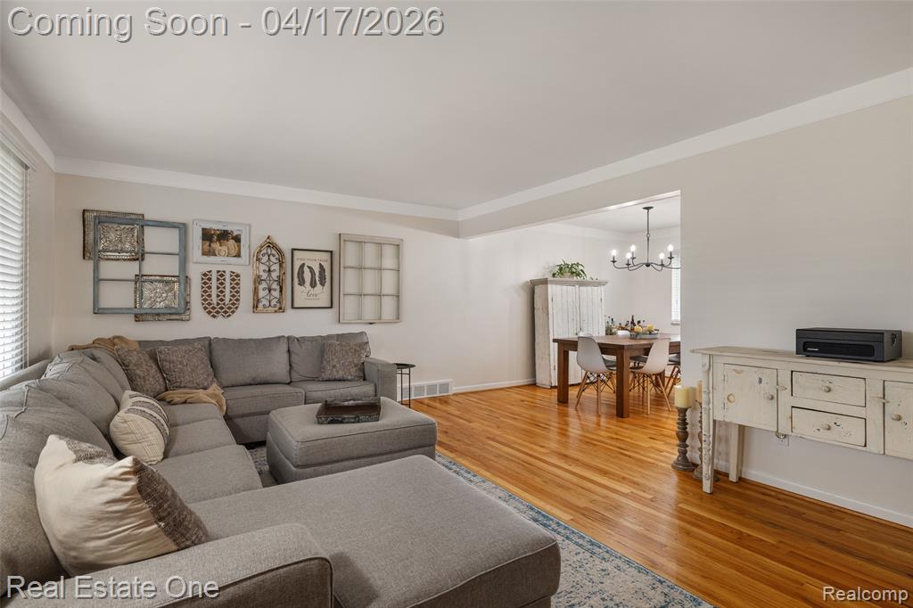 Living room with light wood finished floors, crown molding, and hanging lights