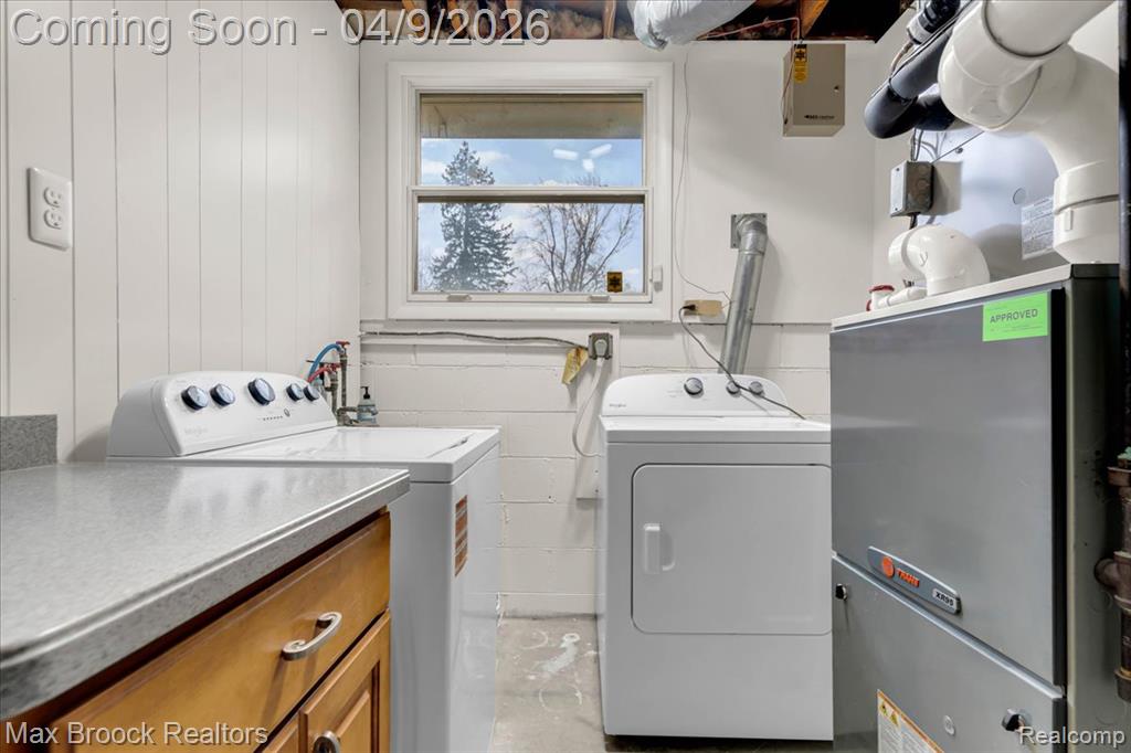Laundry room with heating unit, independent washer and dryer, electric panel, and wooden walls