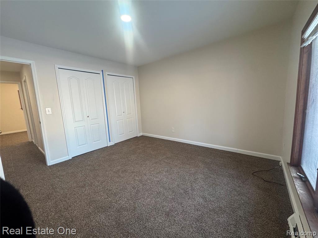 Unfurnished bedroom featuring dark colored carpet and multiple closets
