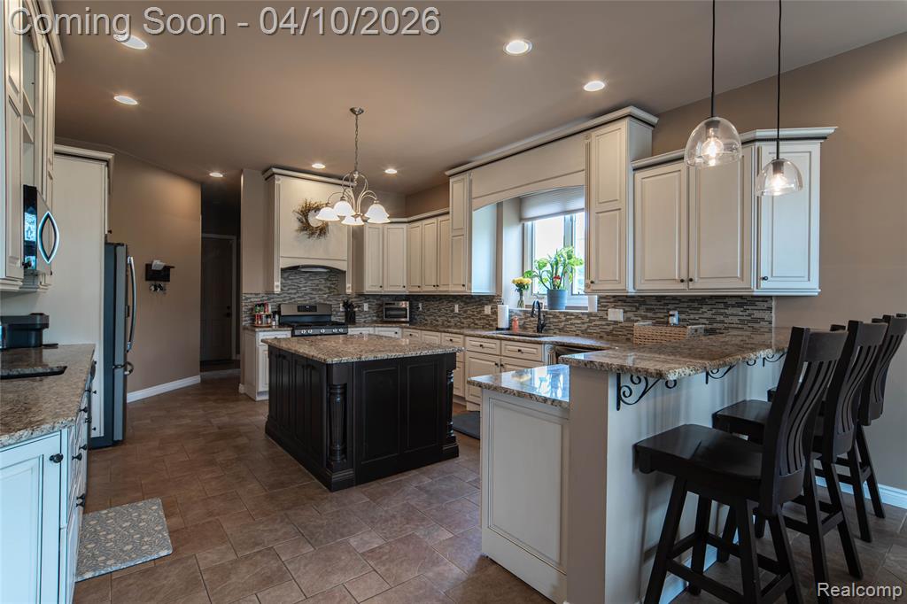 Dual tone kitchen featuring a peninsula, dark stone countertops, a kitchen breakfast bar, stainless steel appliances, and dual tone cabinets