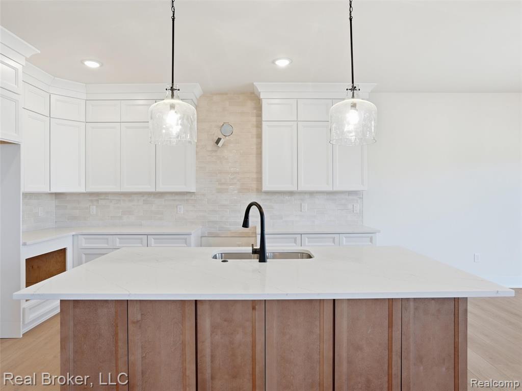 Kitchen with light wood finished floors, an island with sink, light stone countertops, decorative light fixtures, and dual tone cabinetry