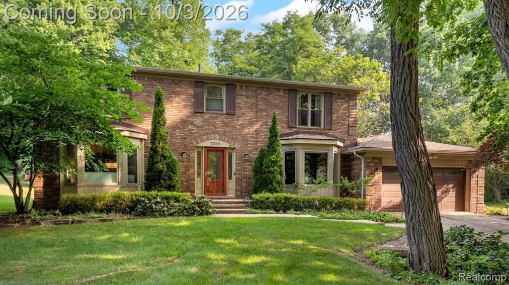 Brick Colonial residence showcasing a symmetrical facade with paired evergreen landscaping, manicured lawn, and mature shade trees