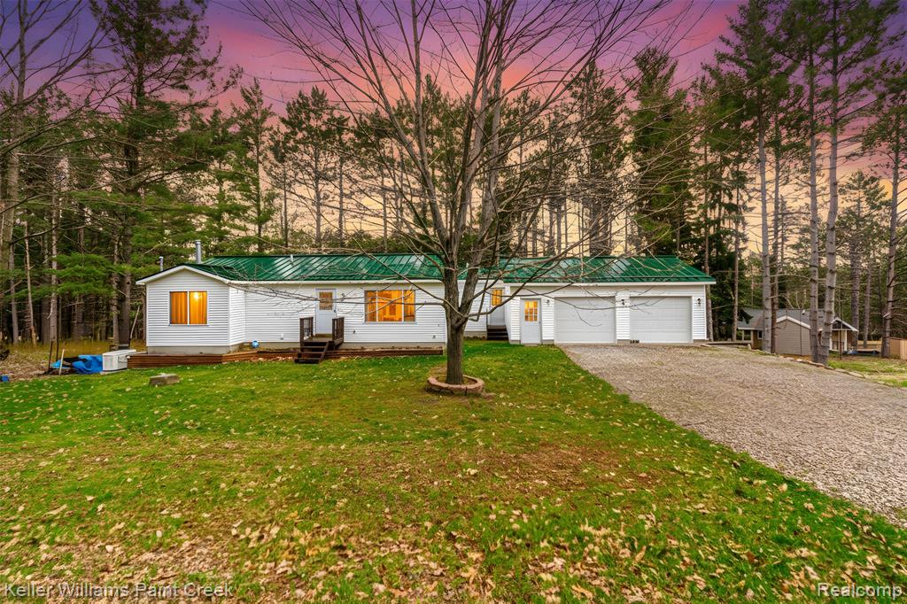 View of front of house featuring driveway, a metal roof, a front lawn, view of wooded area, and entry steps