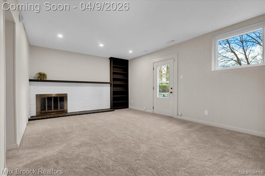 Unfurnished living room with a brick fireplace, light carpet, and recessed lighting
