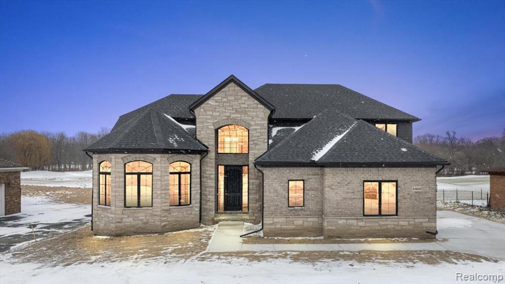 Snow covered back of property featuring stone siding and roof with shingles